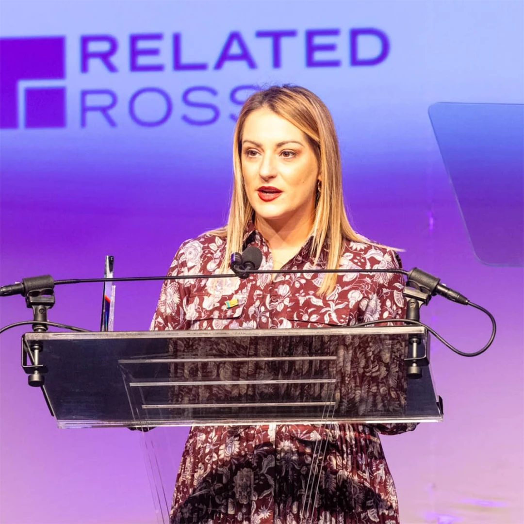 Woman stands at a podium, delivering a speech to an audience.