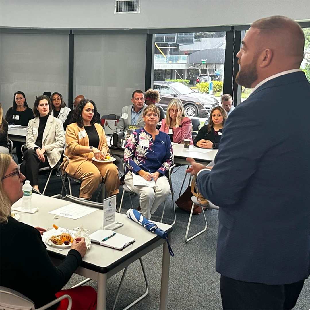 Michael Zeff stands before a group, delivering a presentation and interacting with attentive listeners.